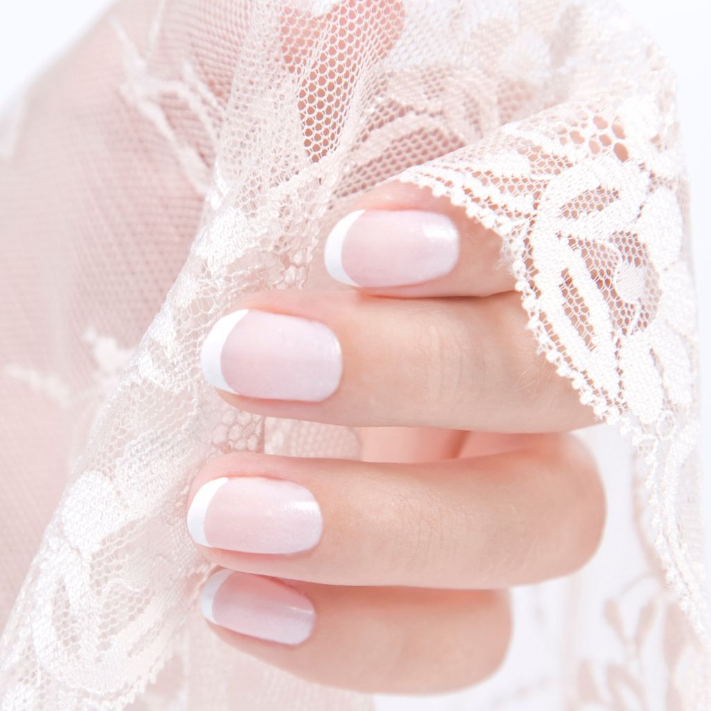 Foto de uñas de novia rosas y blancas mientras sostiene el belo de su vestido