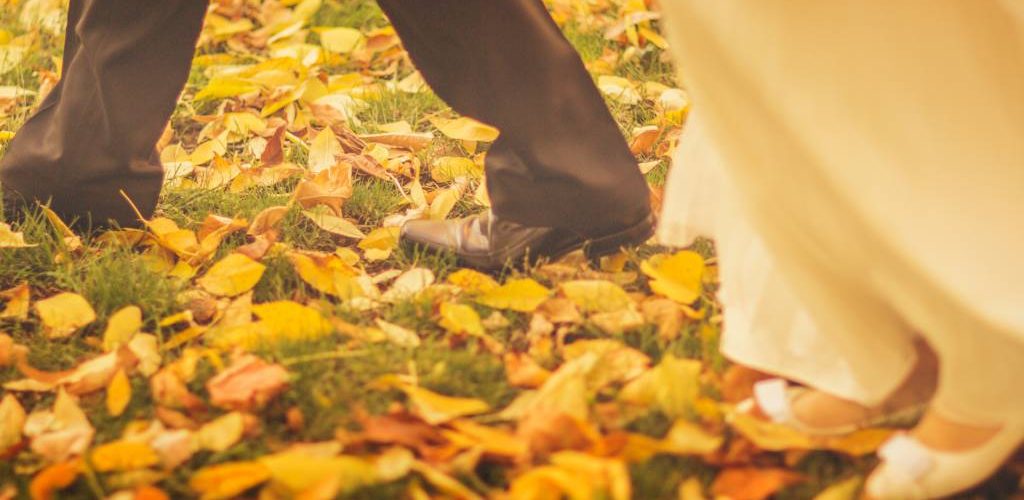 novia y novia caminando por las hojas naranjas en una boda de otoño